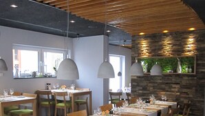 Un restaurante con mesas y sillas de madera, manteles blancos y lámparas colgantes.