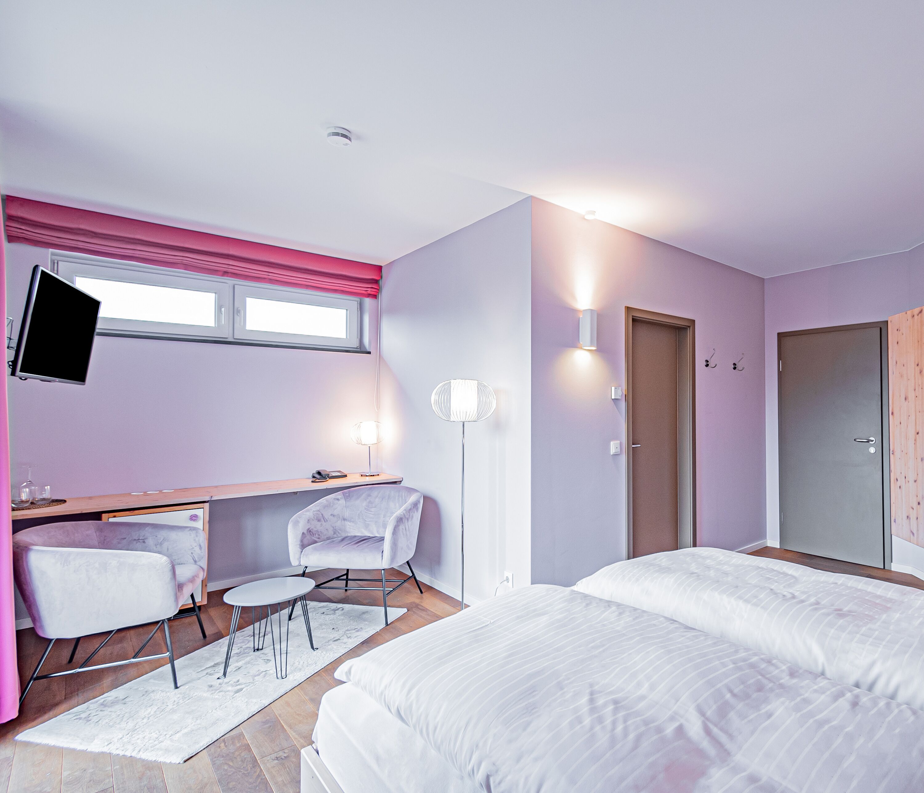 Un dormitorio moderno con escritorio, dos sillas, cama y armario.