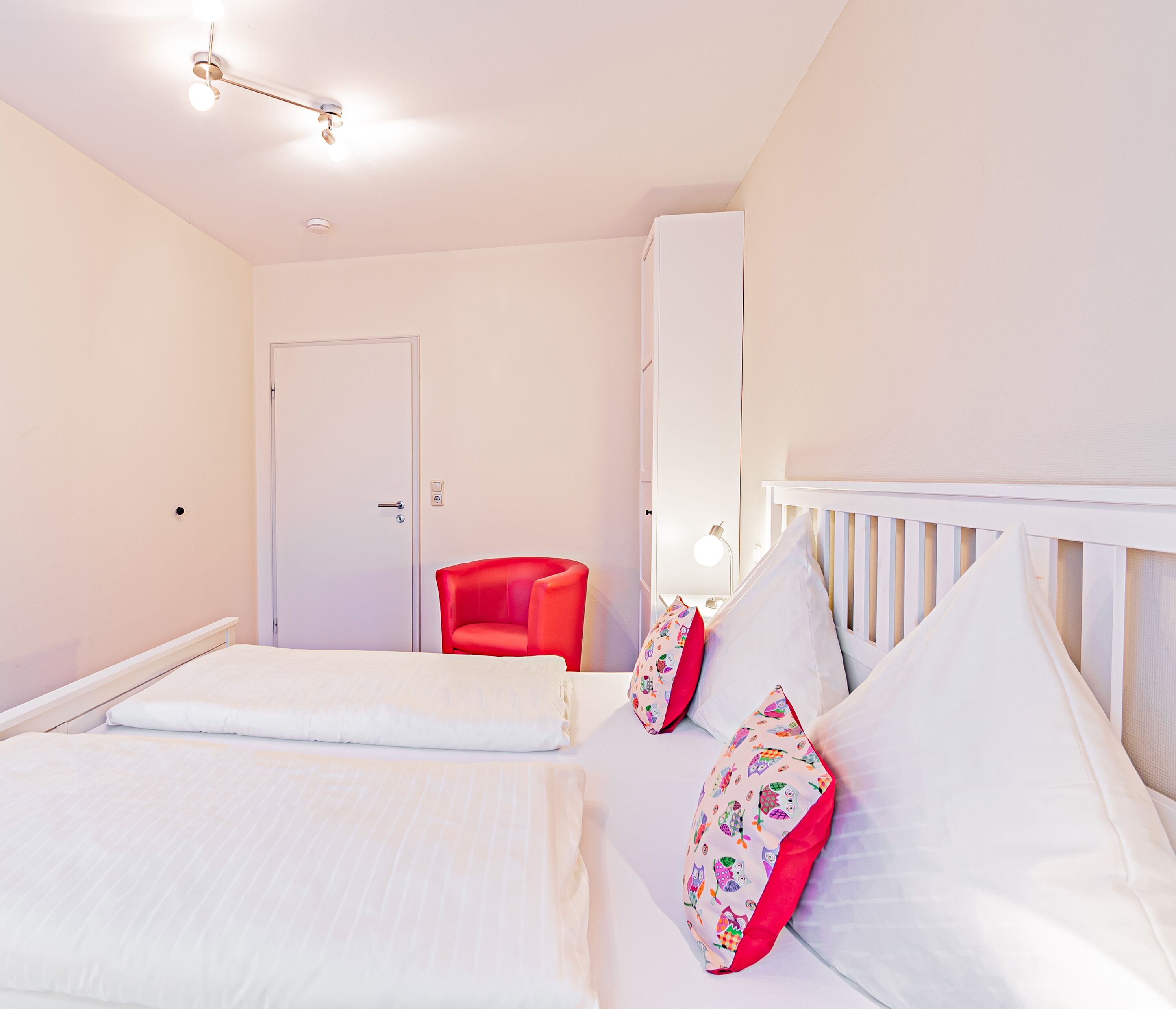 Un dormitorio con una cama, una silla roja, una cuna blanca y una puerta.