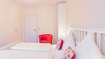 Un dormitorio con una cama, una silla roja, una cuna blanca y una puerta.
