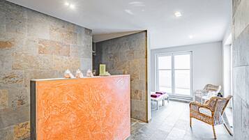 Un espace d’accueil avec un mur en pierre, un comptoir de réception, des fauteuils en osier et une grande fenêtre.