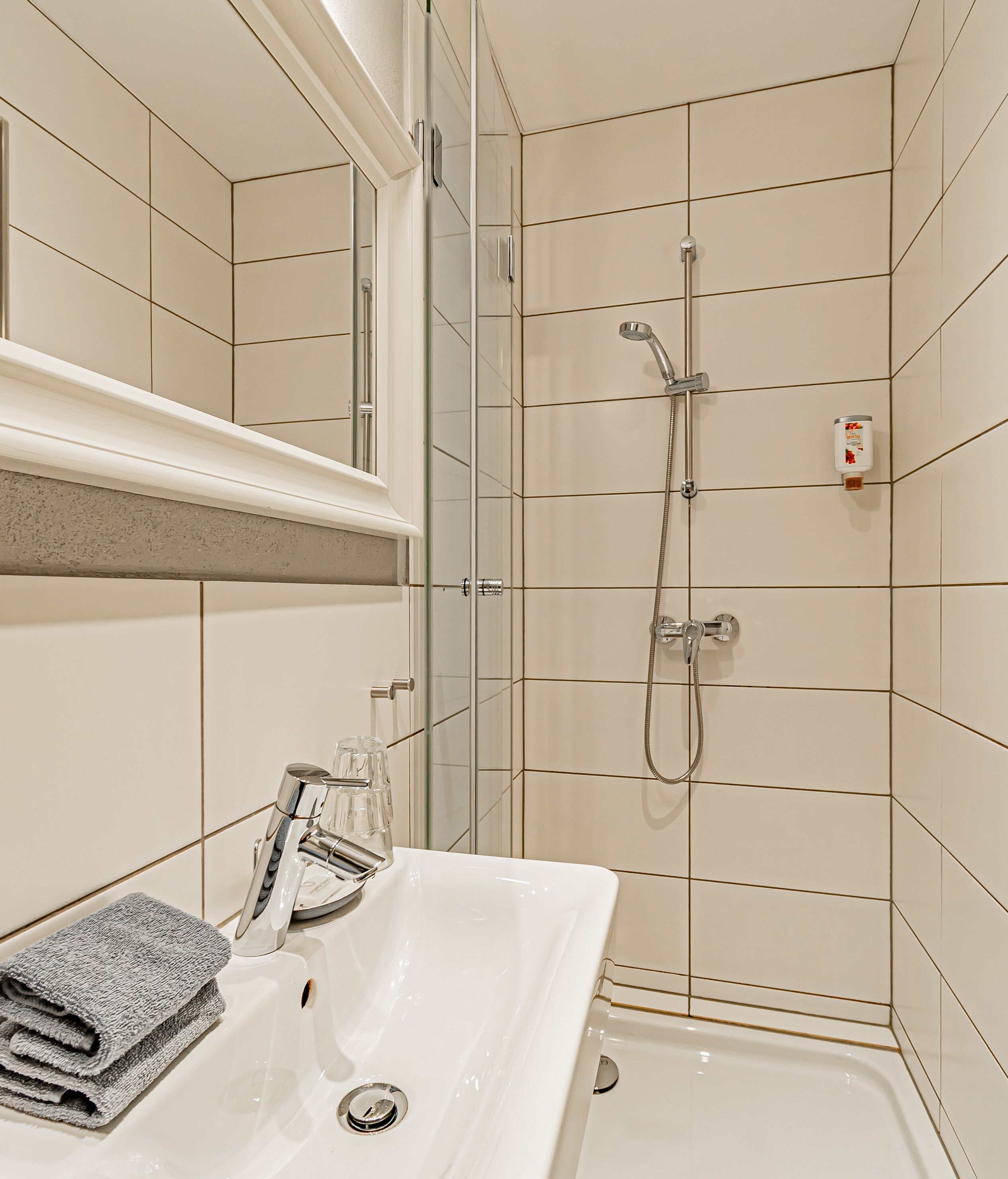 Un baño moderno con ducha de vidrio, un lavamanos blanco con una toalla y un espejo sobre el lavamanos.