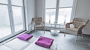 Un cuarto de spa con dos camillas de masaje, una mesita redonda con un vaso y dos sillas de mimbre.