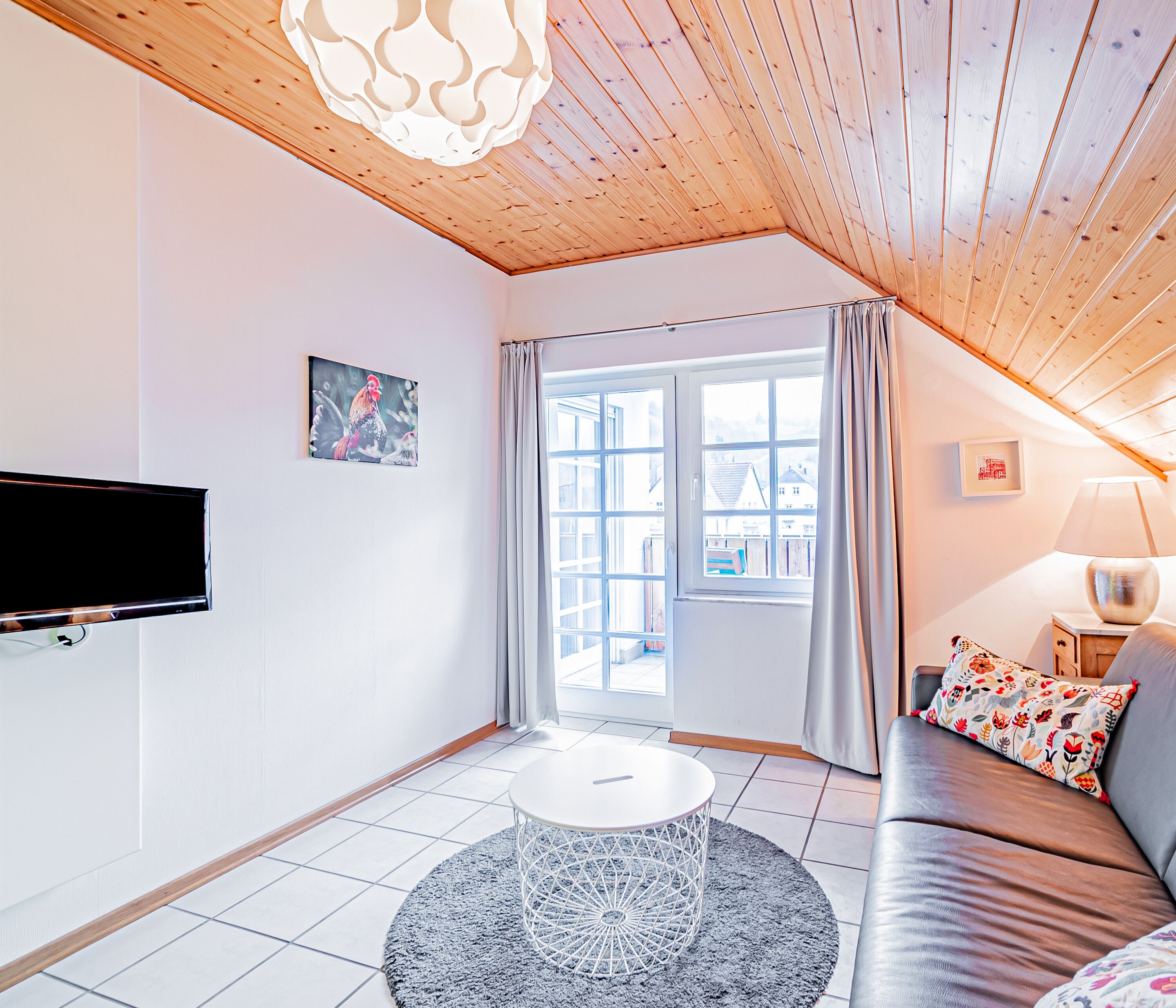 Una sala de estar moderna con techo de madera, una mesa de centro redonda, un sofá, un televisor y una ventana con cortinas.