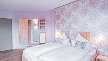 A bedroom with a large bed, wooden headboard, a nightstand, a mirror, and a wall-mounted shelf.