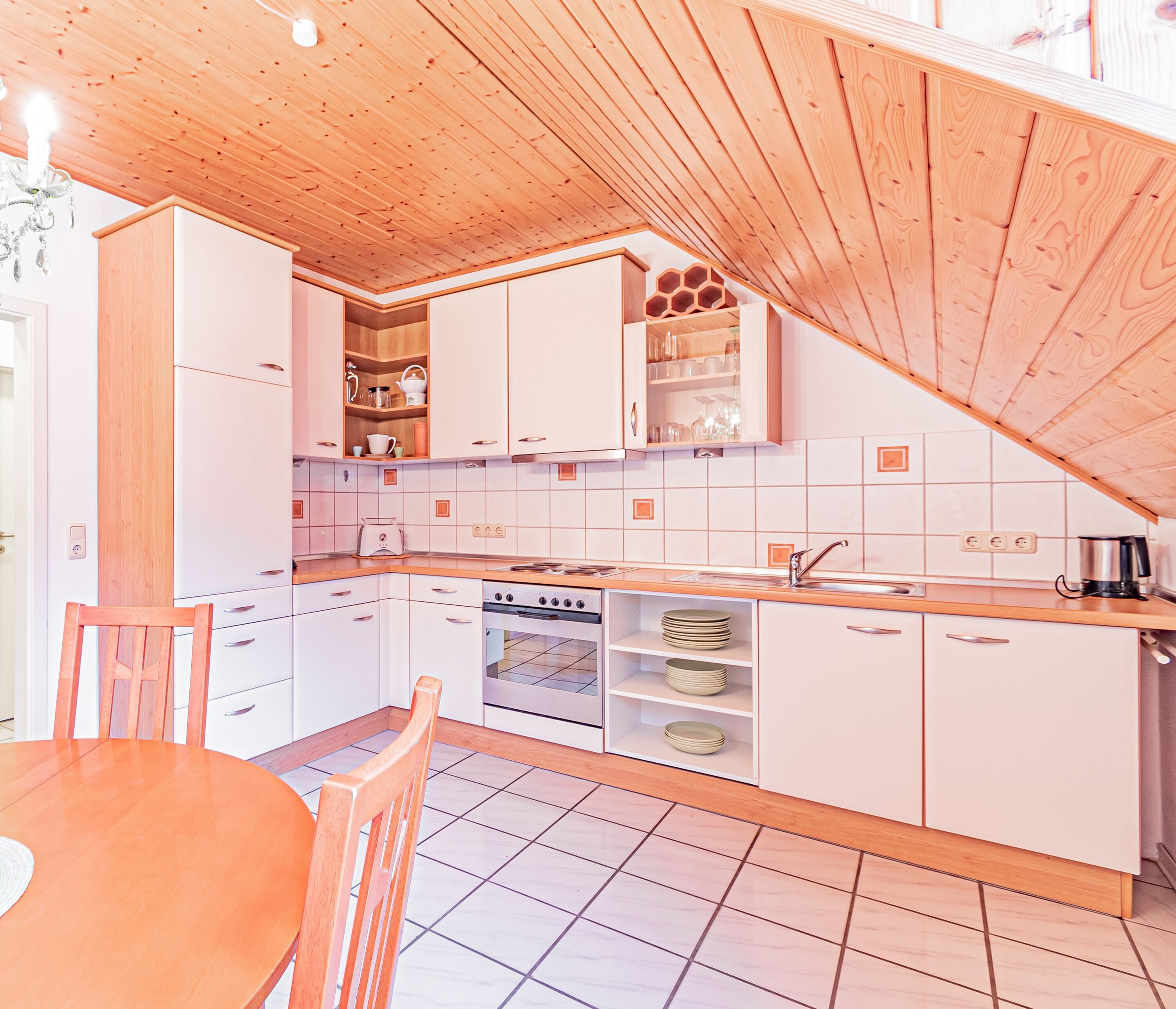 A modern kitchen with white cabinets, a wooden ceiling, and a dining area with a wooden table and chairs.