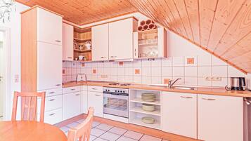 A modern kitchen with white cabinets, a wooden ceiling, and a dining area with a wooden table and chairs.