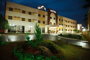 Ein Hotel mit einem markanten Bogenportal und Beschilderung, einem gut beleuchteten Eingangsbereich und angelegten Grünflächen.
