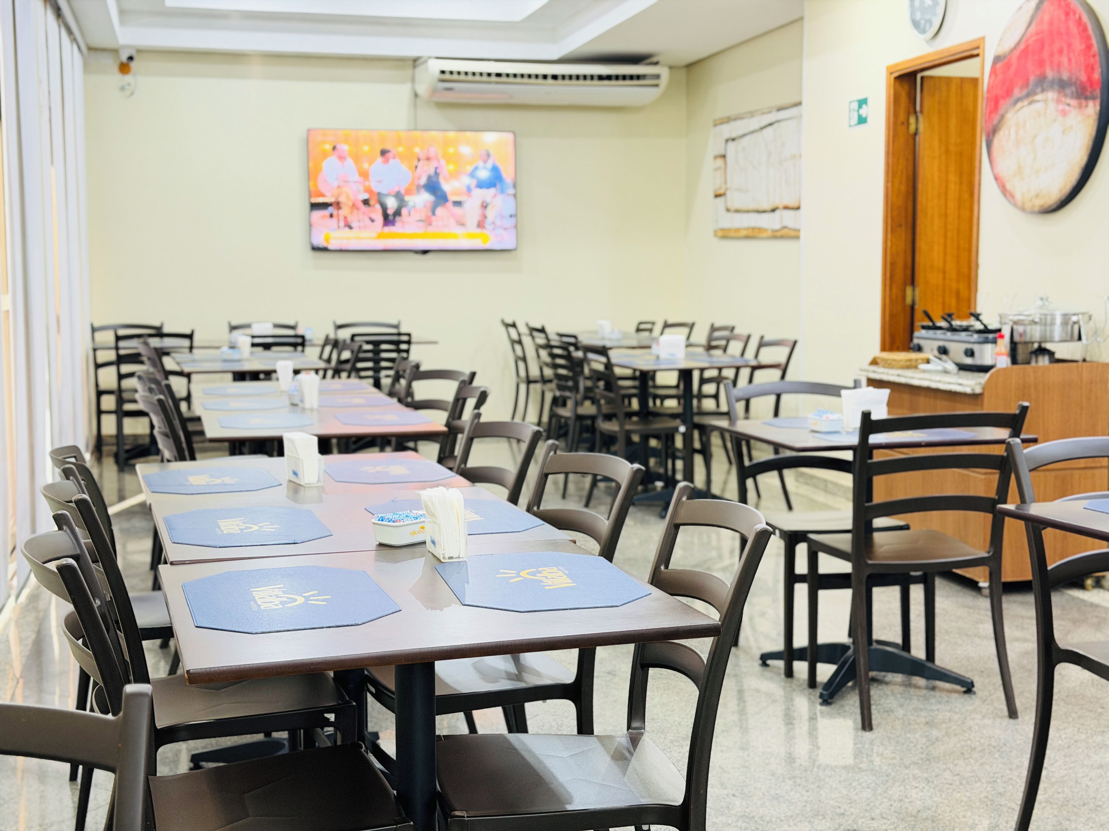 A conference room with tables and chairs, a television screen, and a kitchen area.