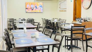 A conference room with tables and chairs, a television screen, and a kitchen area.