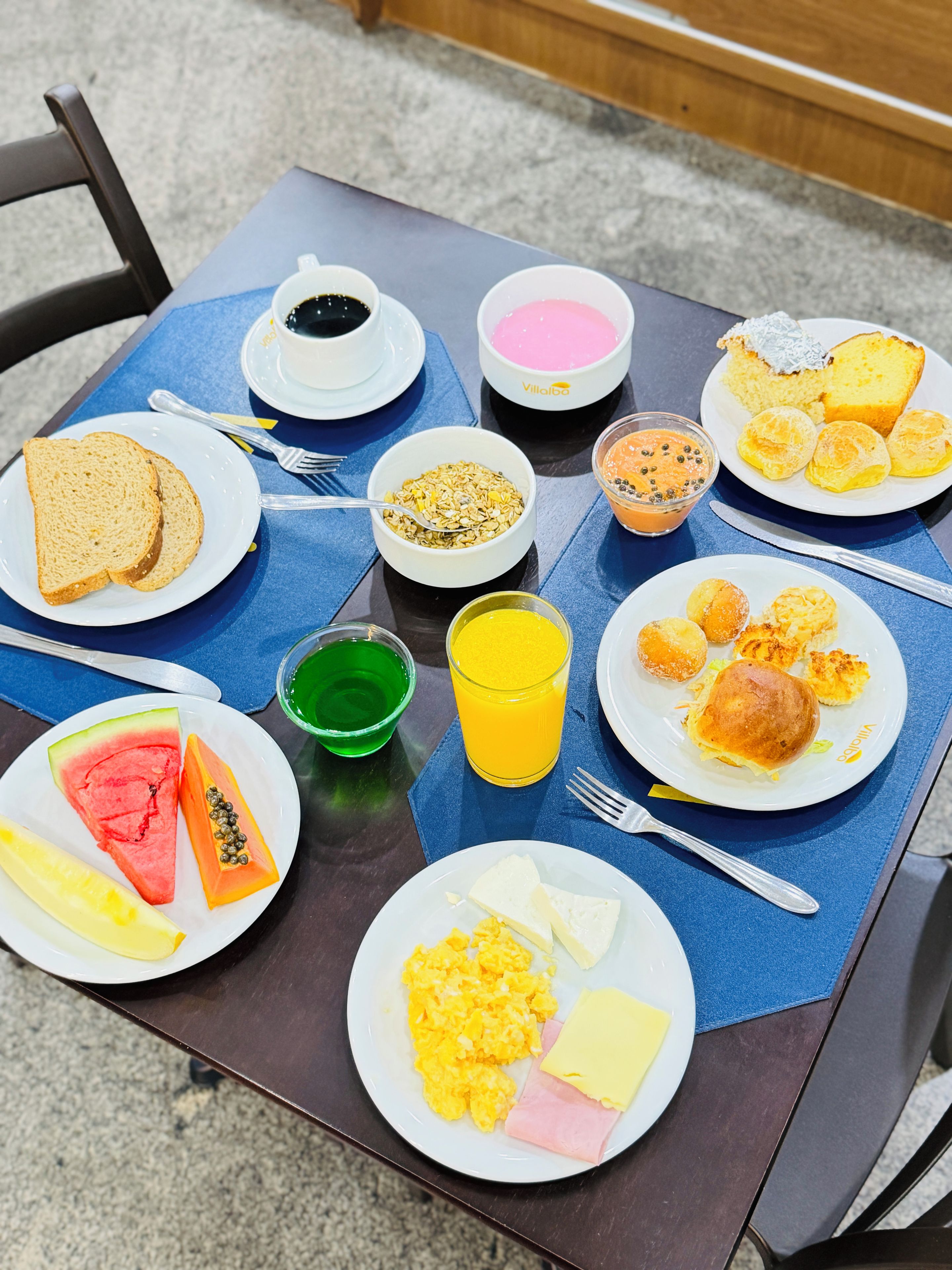 Een ontbijttafel gedekt met toast, roerei, ham en een glas sinaasappelsap.