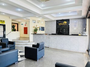 Un hall d’accueil d’hôtel avec un comptoir en marbre noir, un bureau d’accueil et un espace détente avec des chaises bleues.