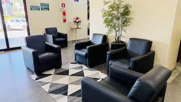 Un área de recepción con sillones de cuero negro, un tapete estampado, una planta en maceta y un extintor.