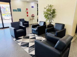 Een receptiegedeelte met zwarte leren stoelen, een kamerbreed tapijt, een potplant en een brandblusser.