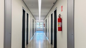 A long, straight hallway with doors on both sides, a fire extinguisher mounted on the wall, and a window at the end. - Villalba Hotel Uberlandia (Uberlandia)
