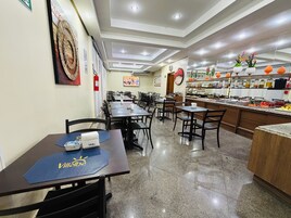 Un comedor de hotel con varias mesas y sillas, una barra de cocina con distintos alimentos, y un extintor en la pared.
