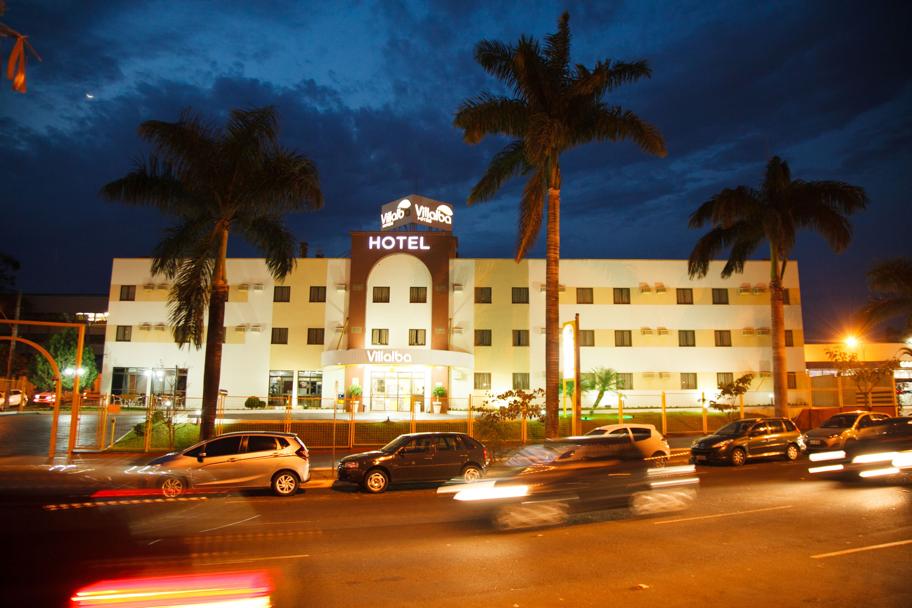 A hotel with a prominent 'HOTEL' sign, multiple stories, and a parking lot with several cars.