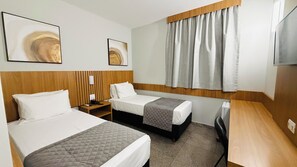 A hotel room with two beds, a desk, a TV, and artwork on the walls.
