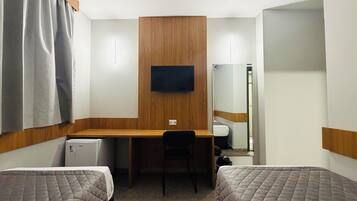 A hotel room with a wooden desk, two beds, a chair, a television, and a small refrigerator.