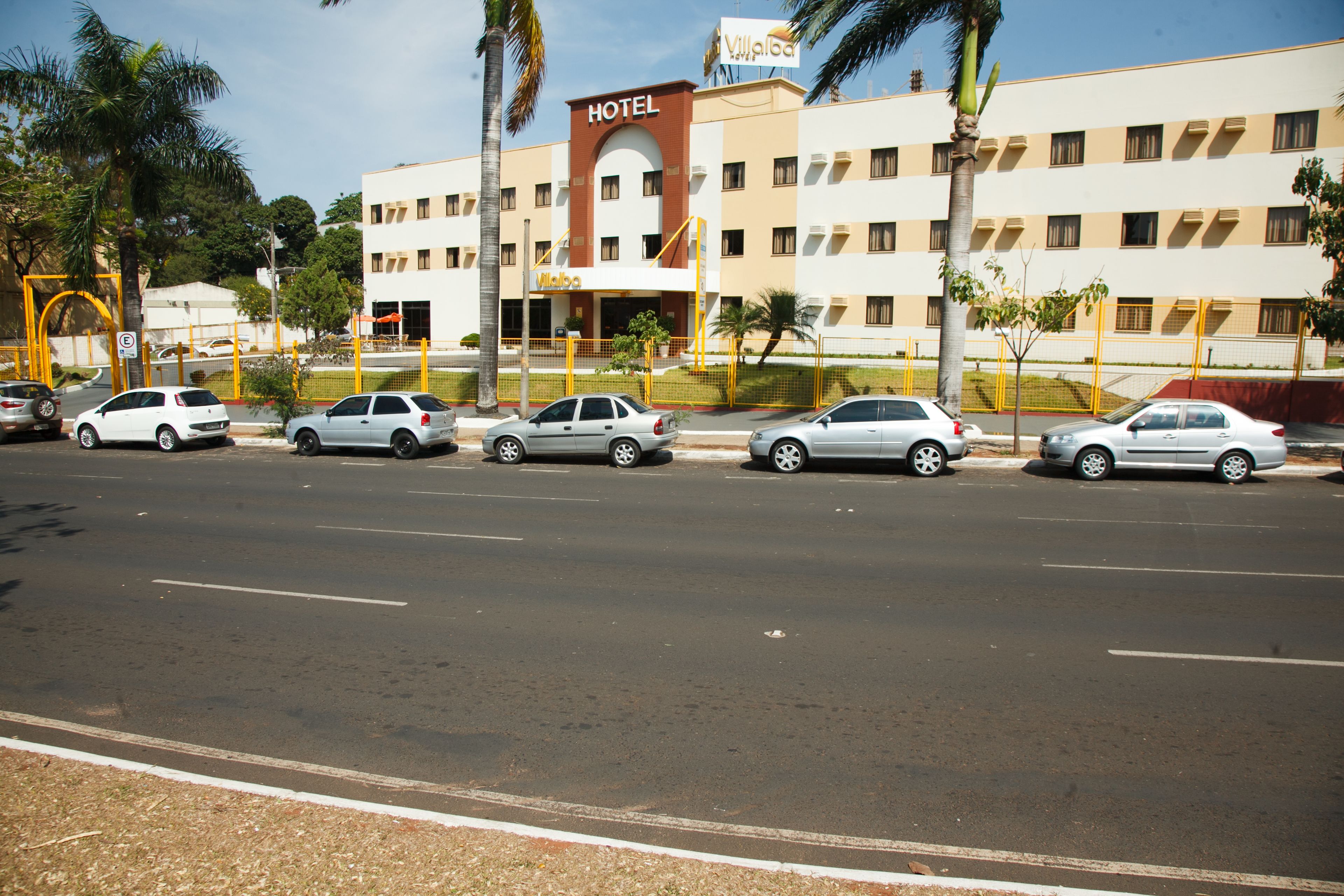 Un hotel con entrada principal, varios pisos y un estacionamiento con varios coches.