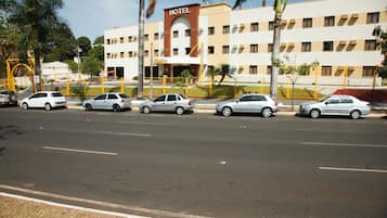 Un hotel con entrada principal, varios pisos y un estacionamiento con varios coches.
