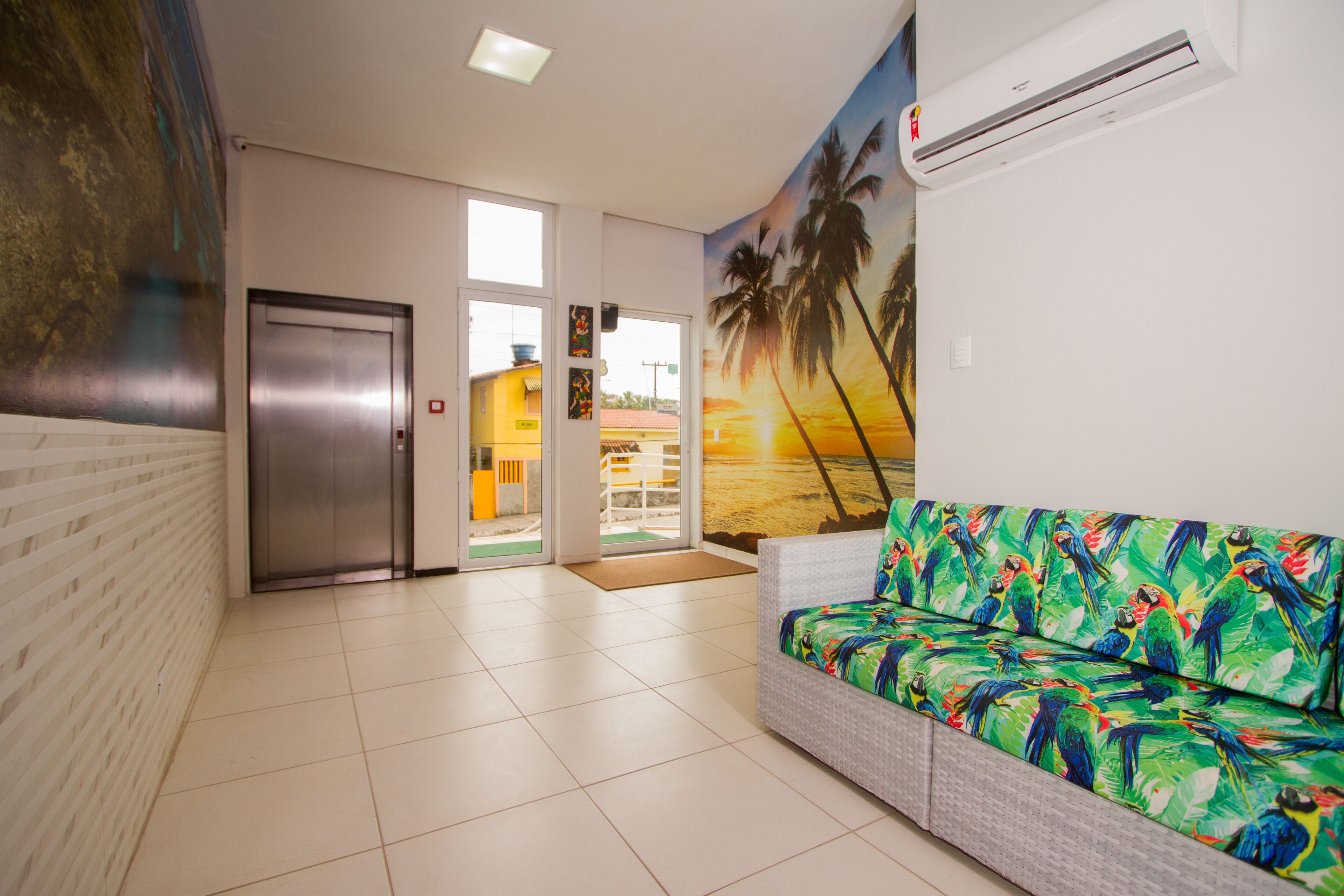 A reception area with a sofa, an elevator, and a mural of palm trees.