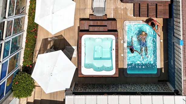 An aerial view of a rooftop pool area with multiple hot tubs, lounge chairs, and umbrellas. - Pousada Marie Claire Flats (Ipojuca)
