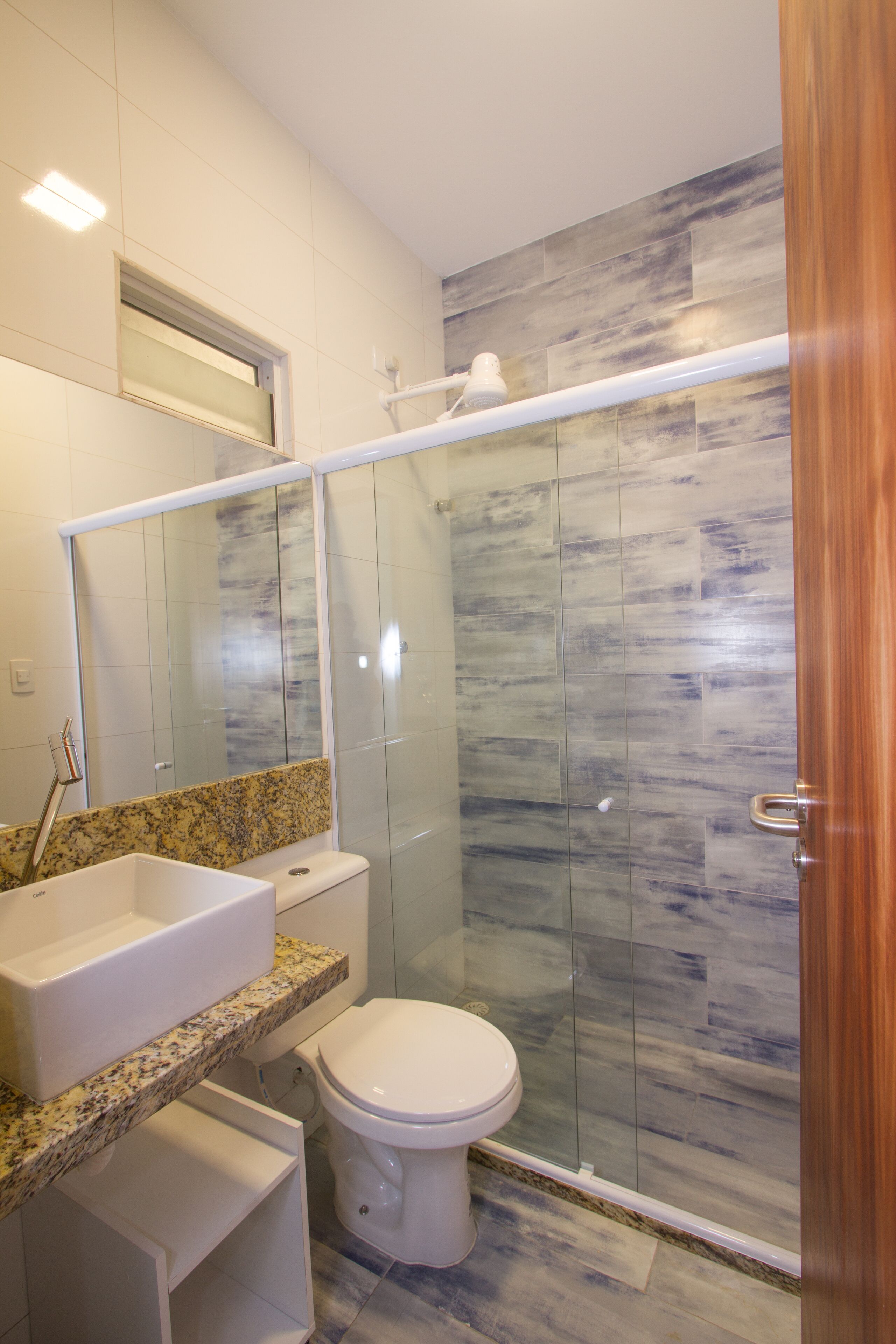 A modern bathroom with a glass-enclosed shower, a white toilet, a granite countertop sink, and a large mirror.