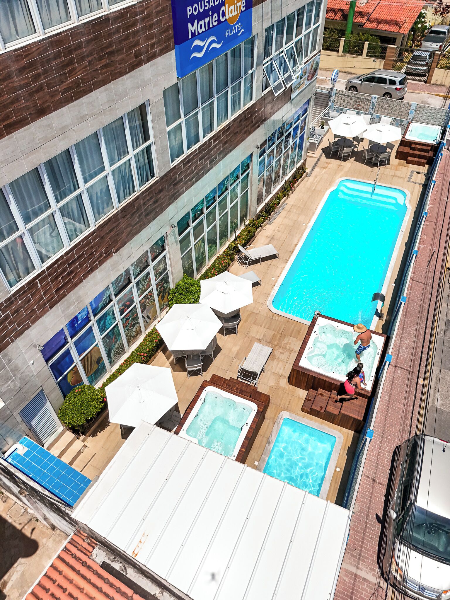 A rooftop pool area with multiple hot tubs, lounge chairs, and umbrellas.
