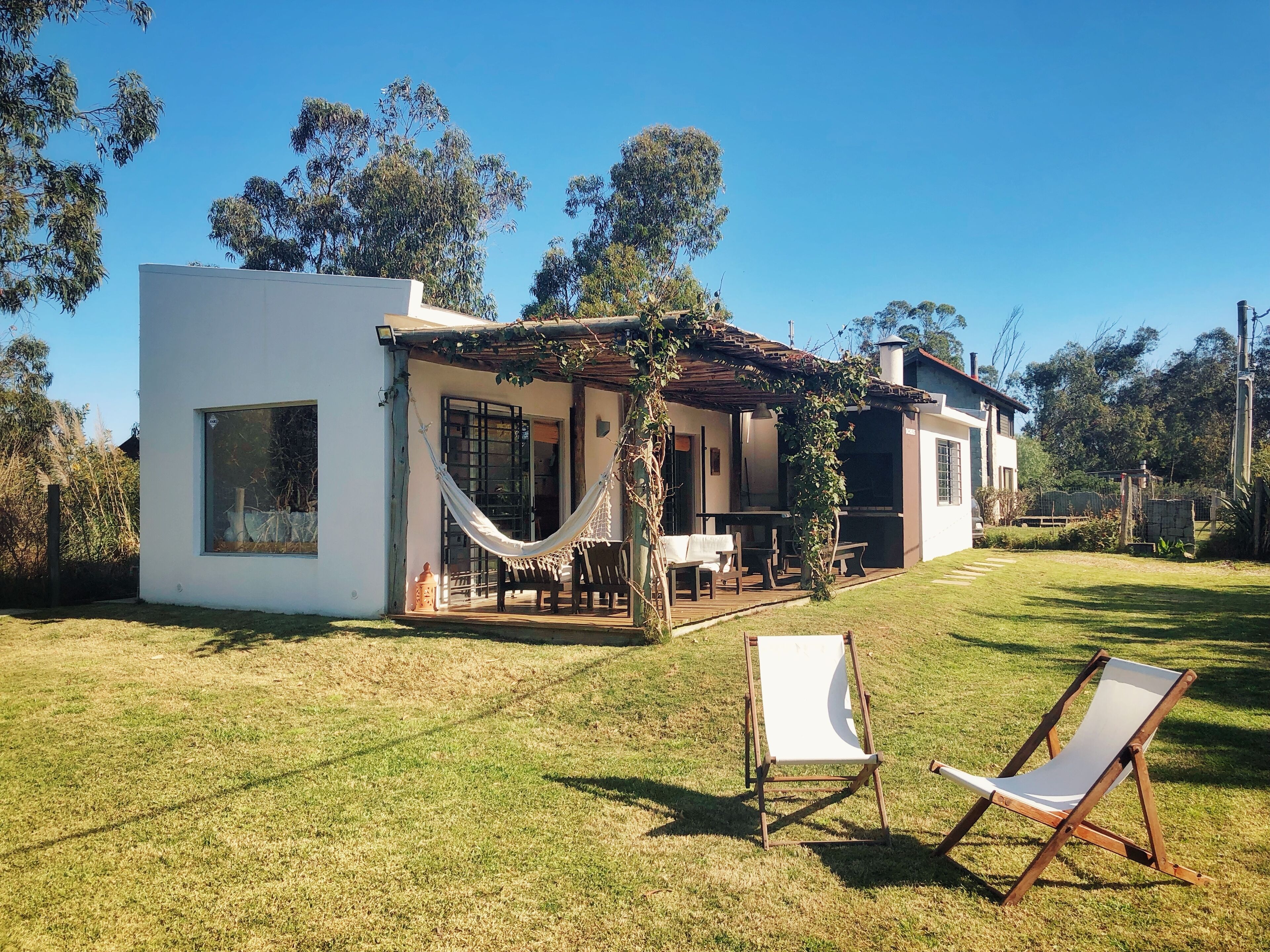 A modern house with a patio, a hammock, and two lounge chairs.