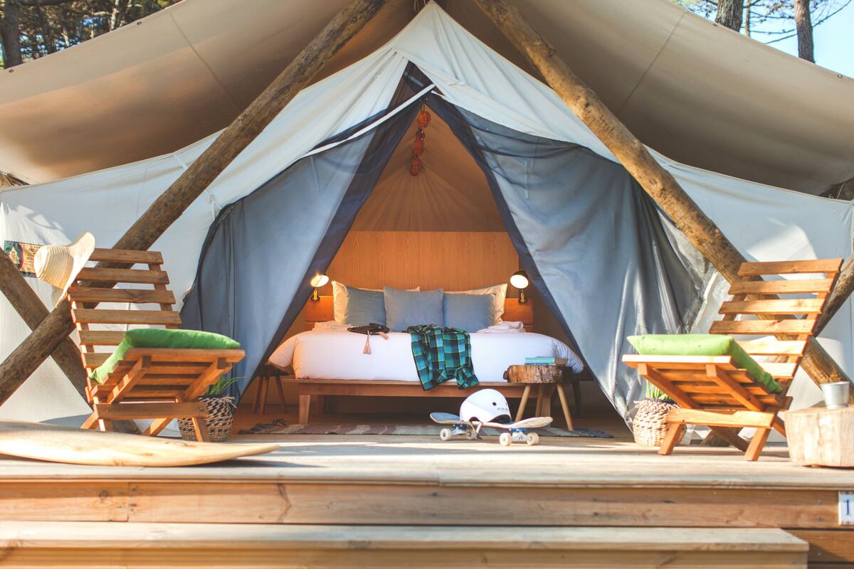 A tent with a bed, two chairs, a table, and a skateboard.