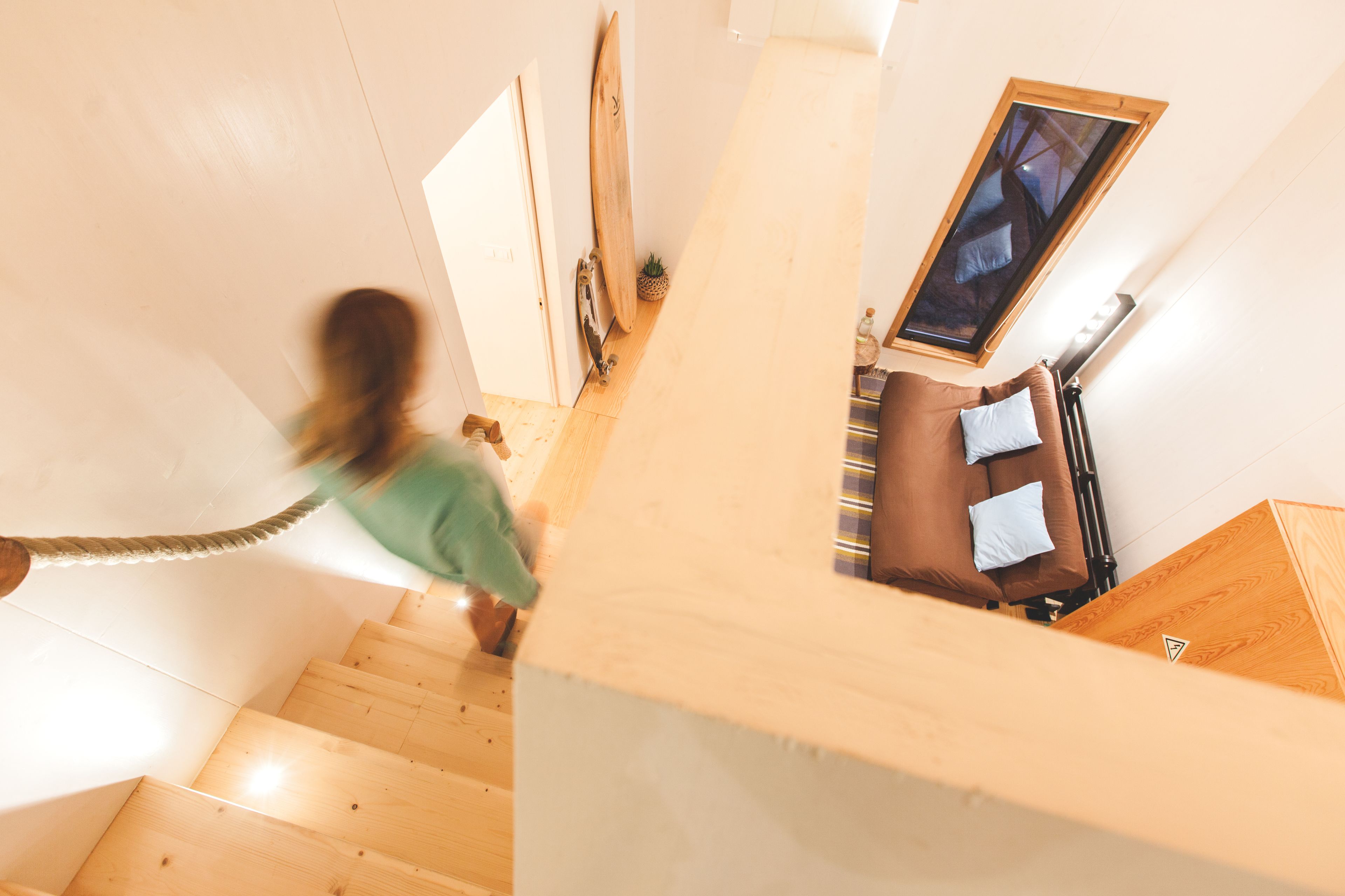 A wooden staircase leading to a room with a bed, a window, and a small plant.