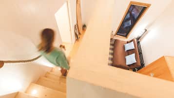 A wooden staircase leading to a room with a bed, a window, and a small plant.