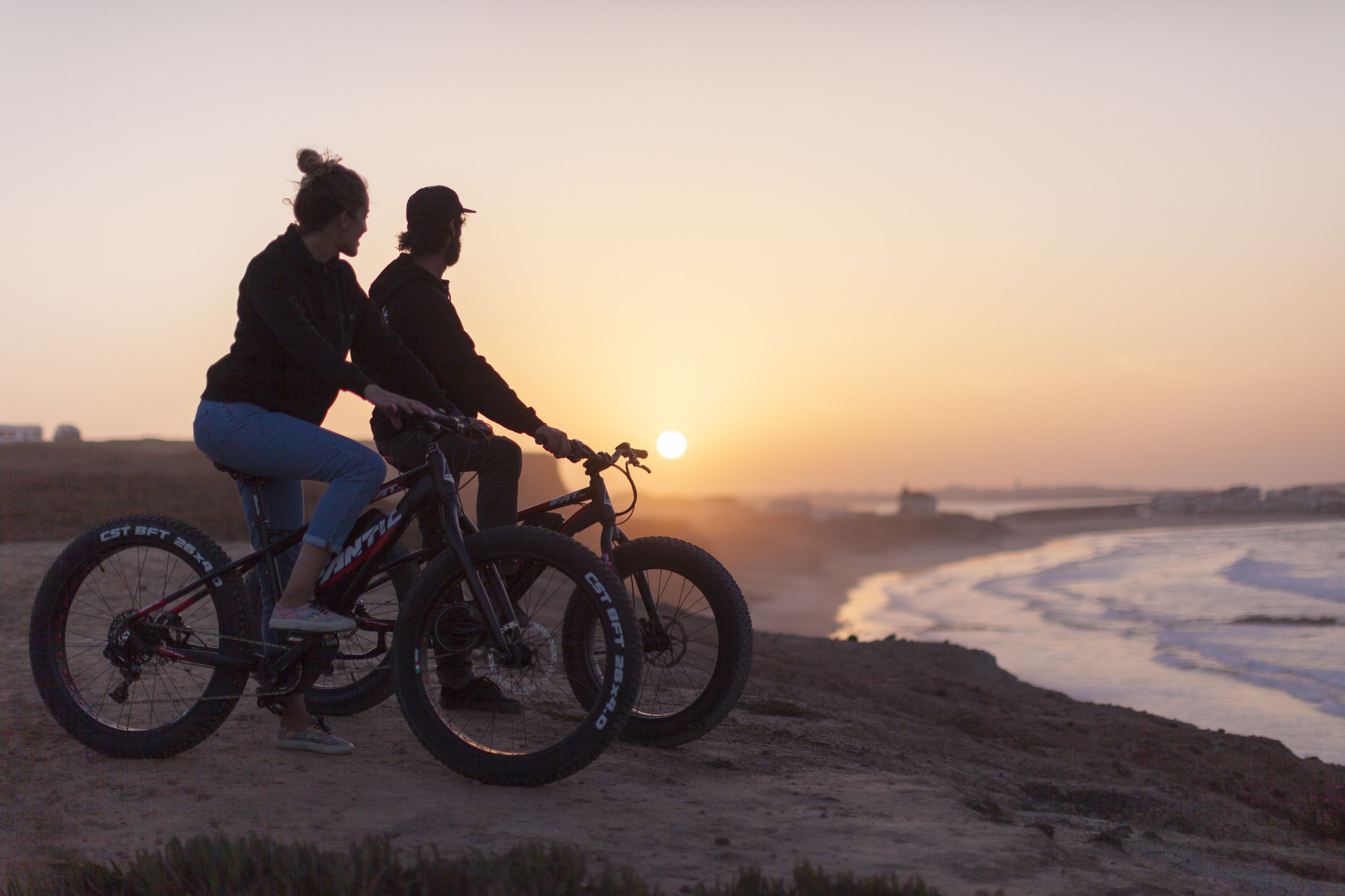 Deux personnes à vélo sur une plage de sable au coucher du soleil.