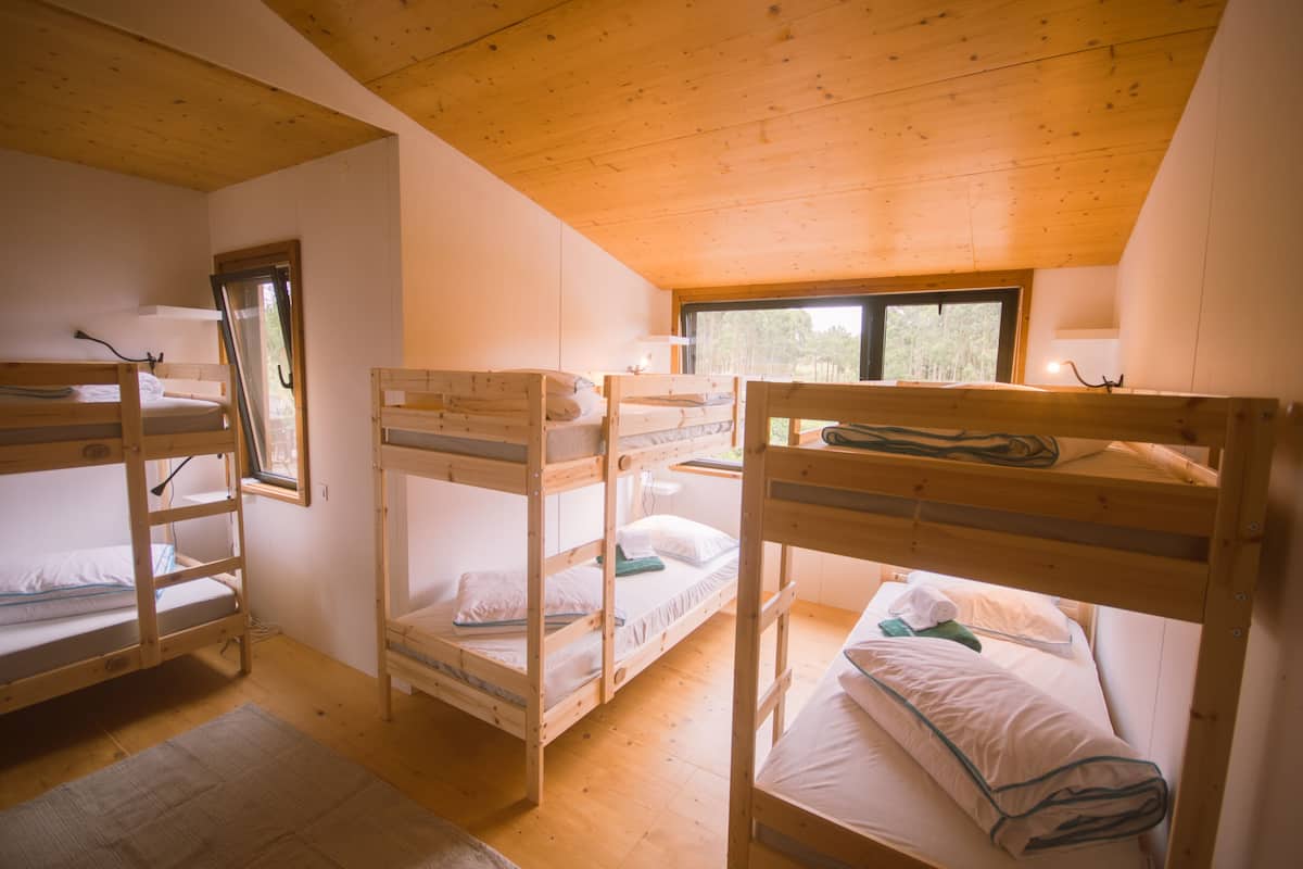 A dormitory room with bunk beds, wooden ceilings, and a window providing natural light.