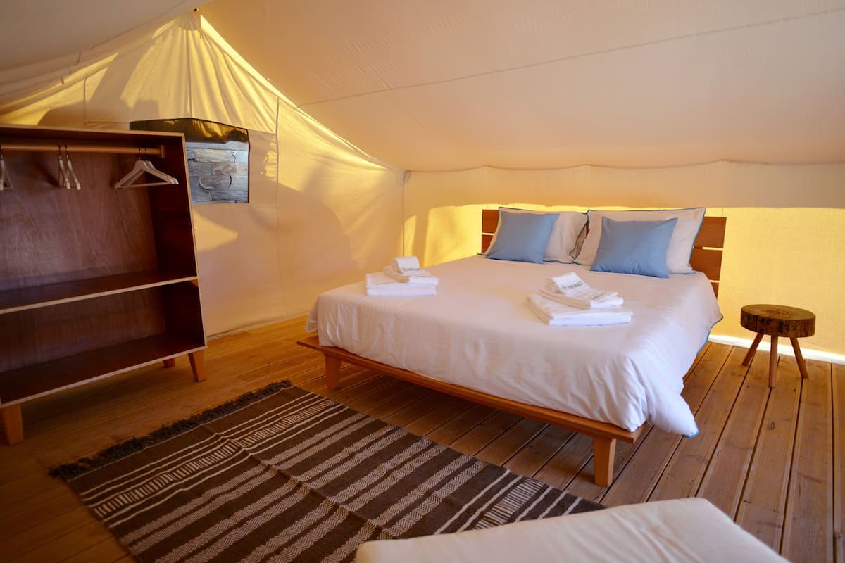 A tented room with a bed, wooden wardrobe, and a small stool.