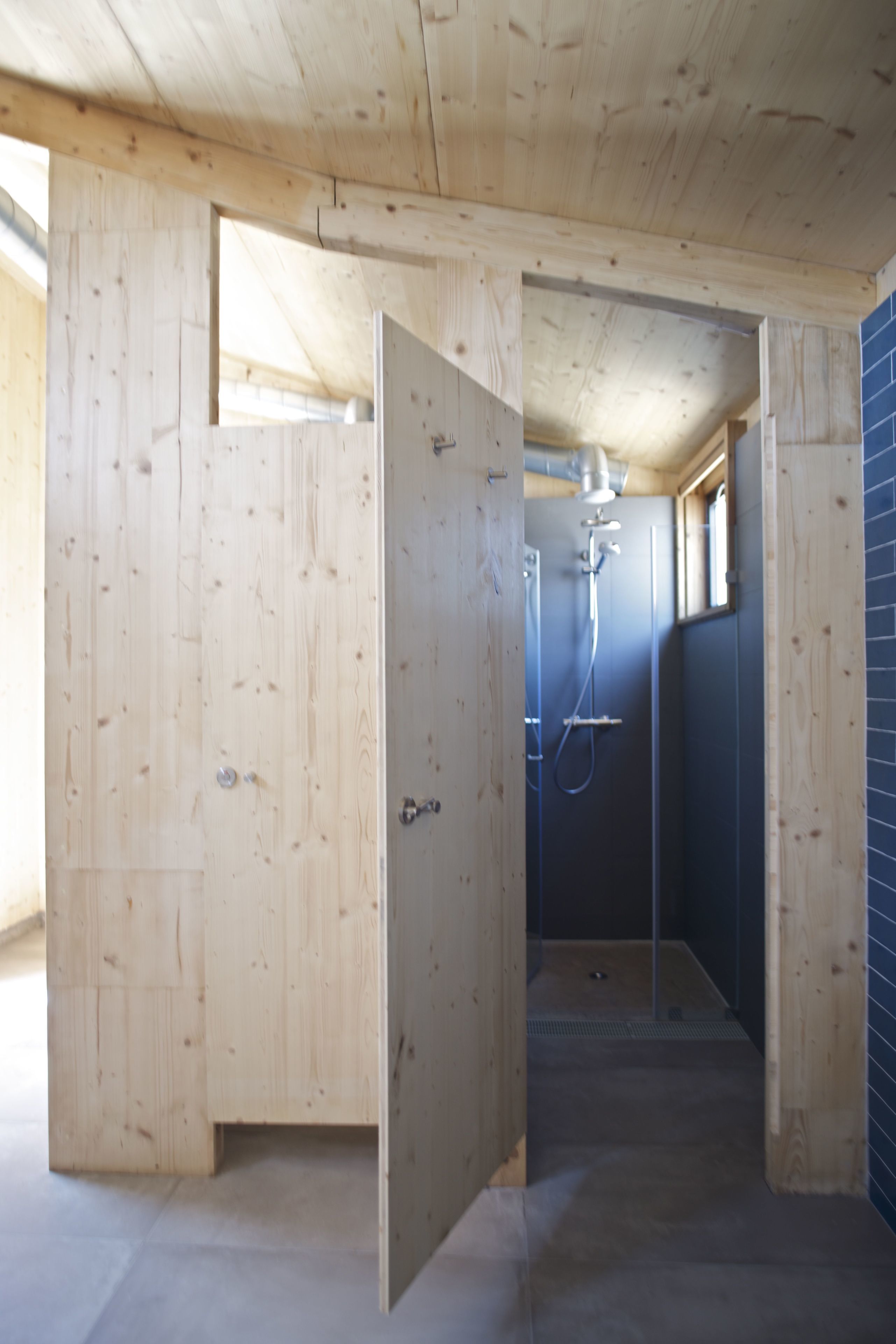 Un interior de madera con zona de ducha, paredes de madera y suelo de baldosas.