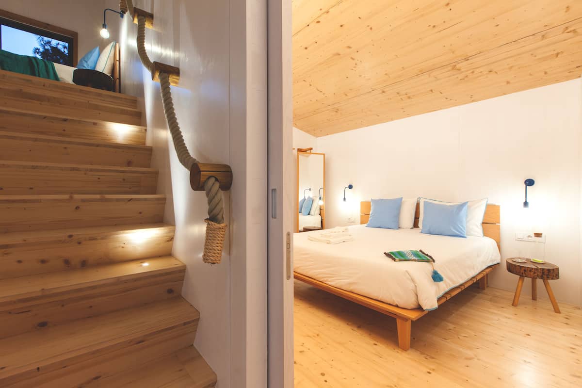 A wooden staircase leading to a bedroom with a bed, bedside tables, and a mirror.