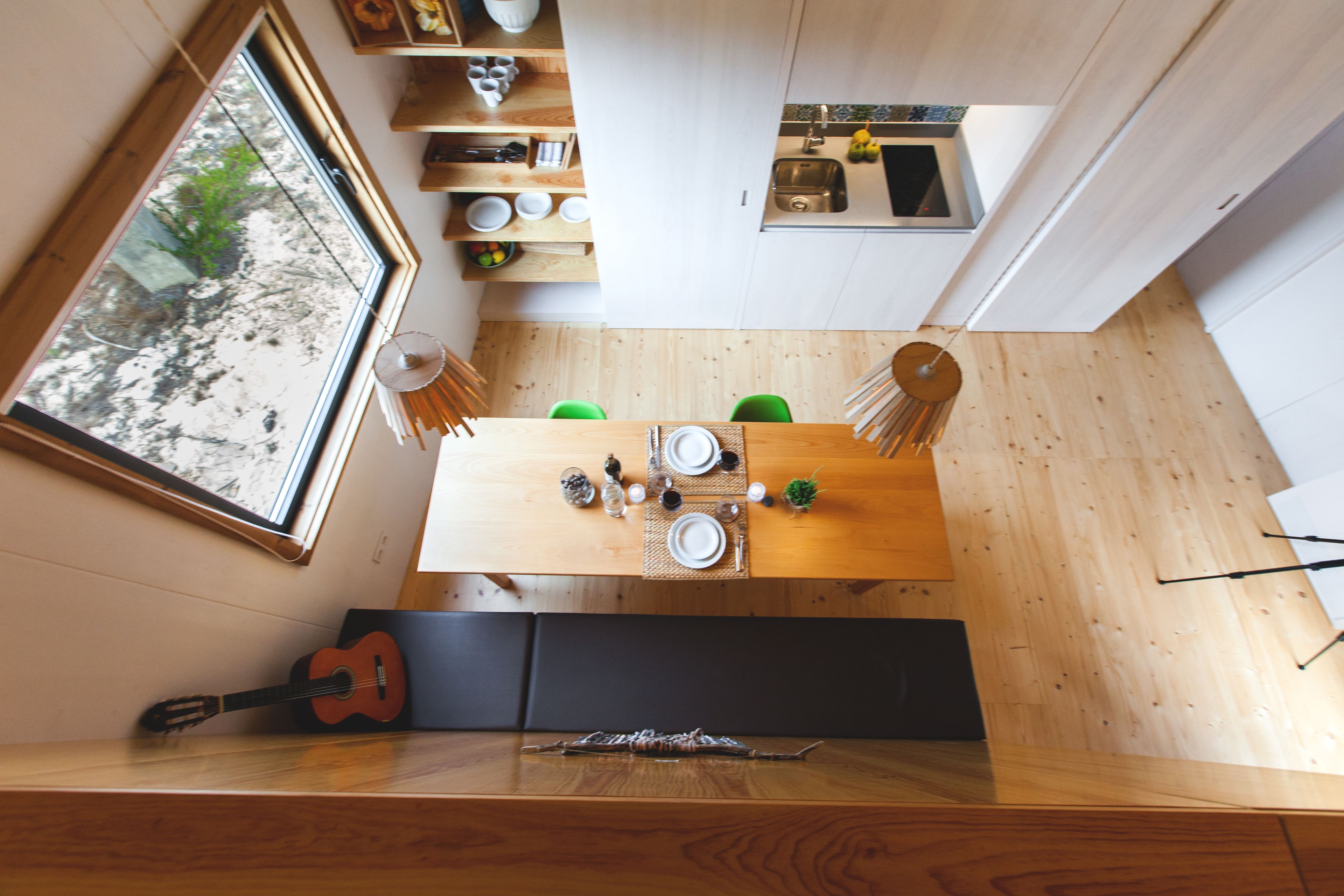 A modern kitchen with a dining area, wooden flooring, and a large window overlooking greenery.