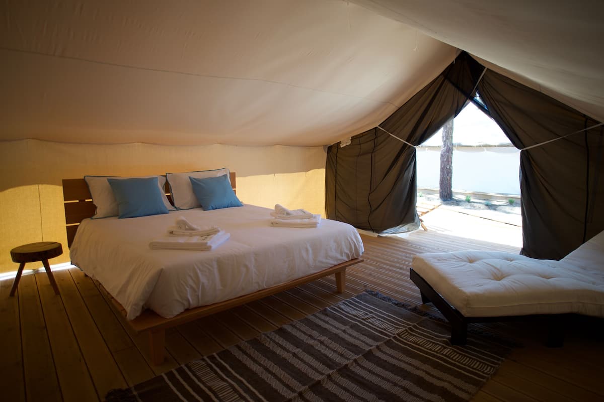 A bedroom with a large bed, a bedside table, a chair, and a view of the sea.