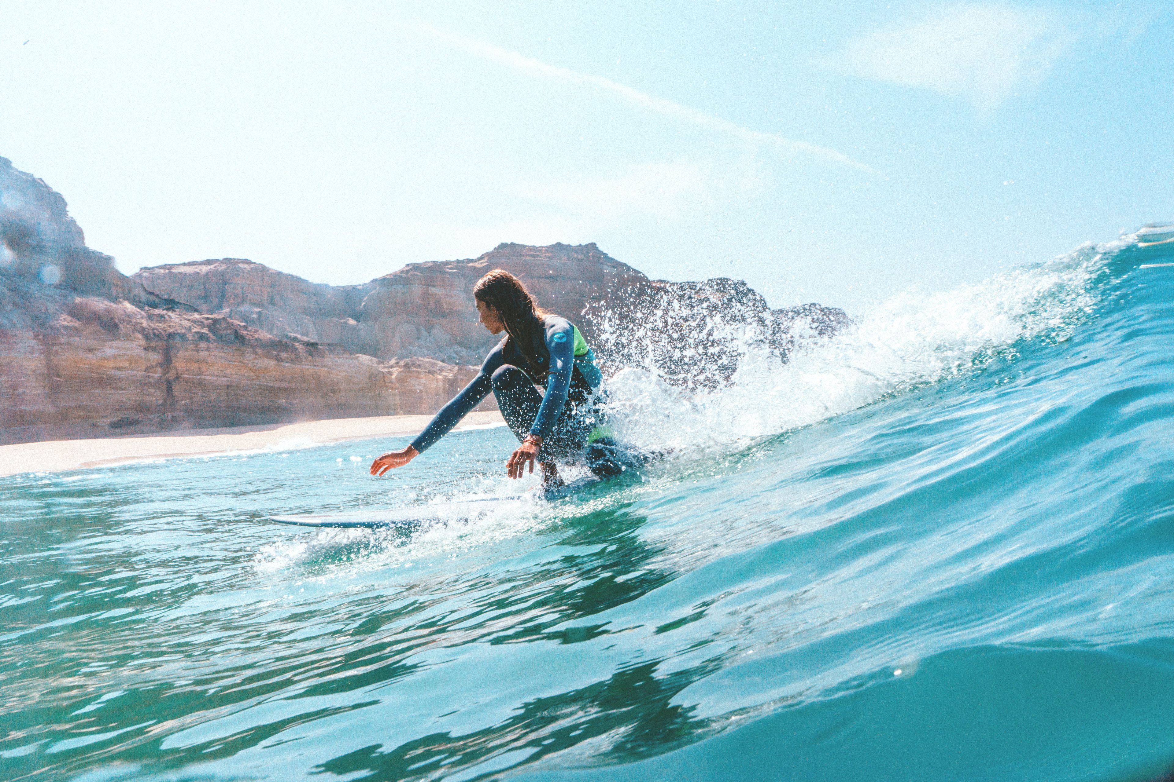 Uma pessoa surfando em uma onda, com uma paisagem rochosa ao fundo.