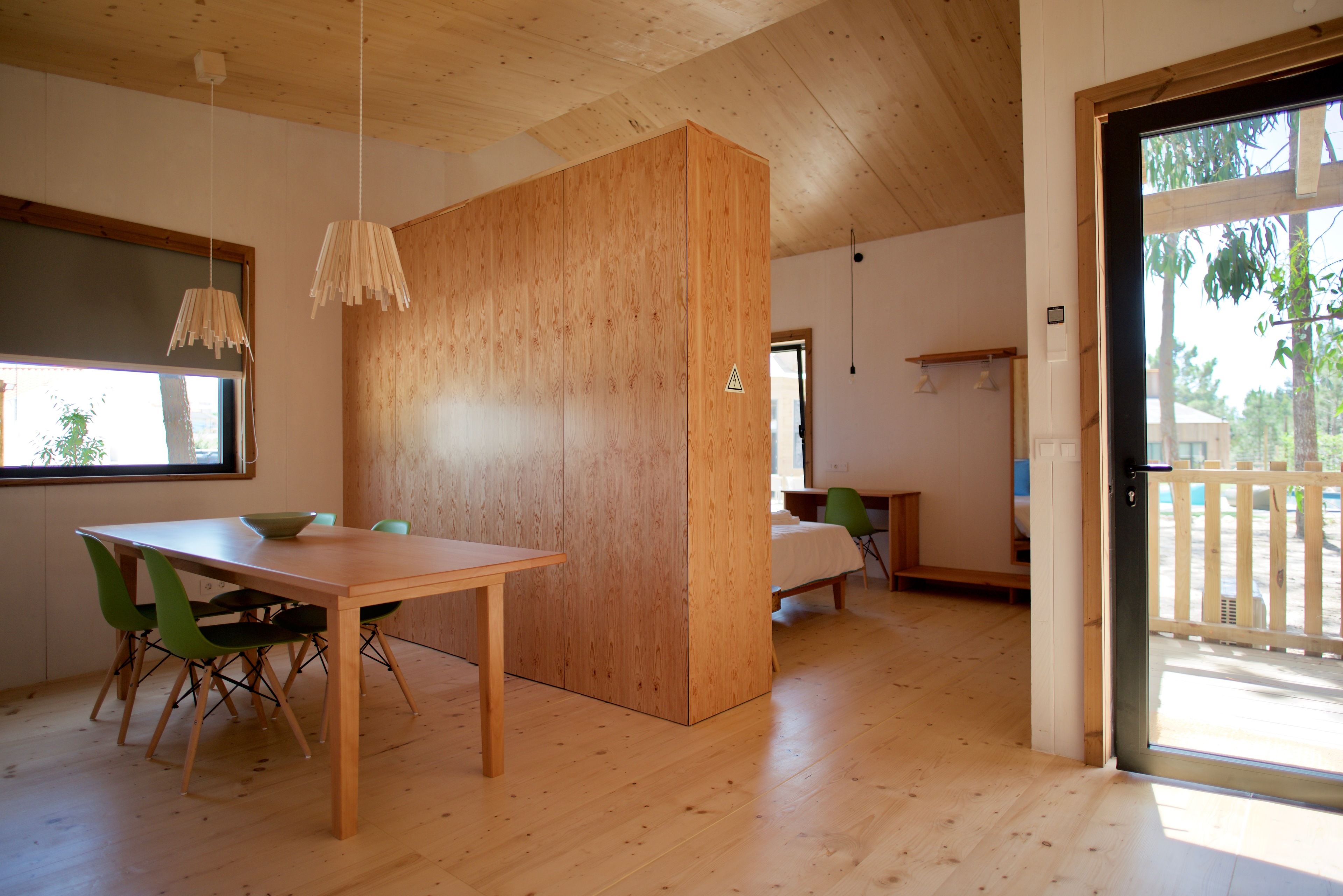 A modern interior with a wooden dining table, green chairs, a wooden partition, and a large window.
