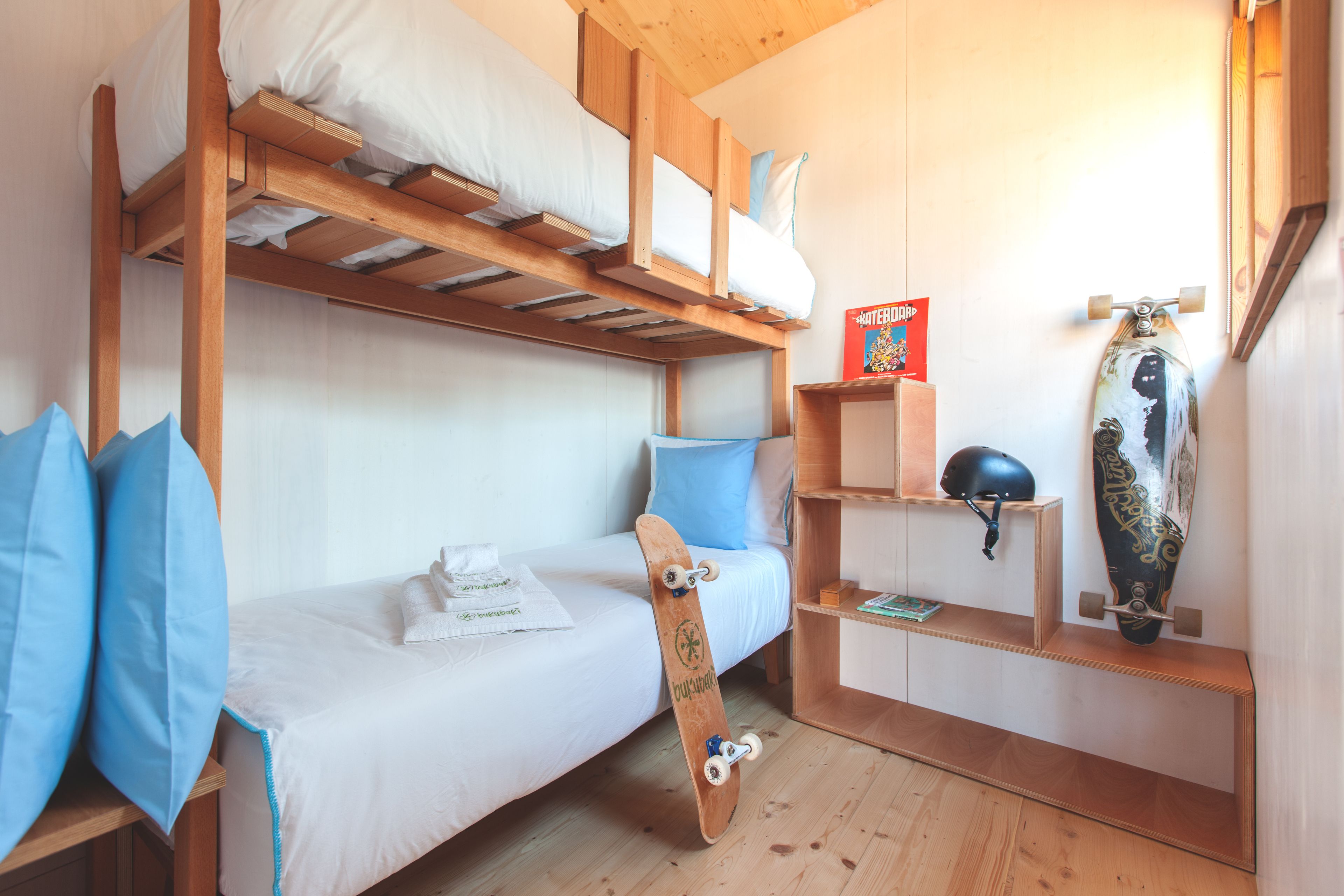 Une chambre avec des lits superposés, un skateboard appuyé contre le mur et un casque posé sur une étagère.