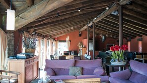 A cozy interior with a wooden ceiling, a sofa, a table with a vase of flowers, and a dining area in the background. - Hotel El Monegal (Guixers)