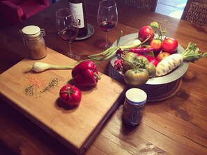 A wooden table with a cutting board, a bowl of fresh vegetables, a bottle of wine, and two glasses. - Hotel El Monegal (Guixers)