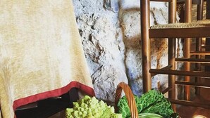 A wicker basket filled with green vegetables on a table with a stone wall background. - Hotel El Monegal (Guixers)