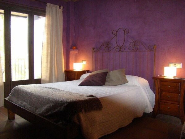 A bedroom with a bed, a nightstand, a lamp, and a window with curtains.