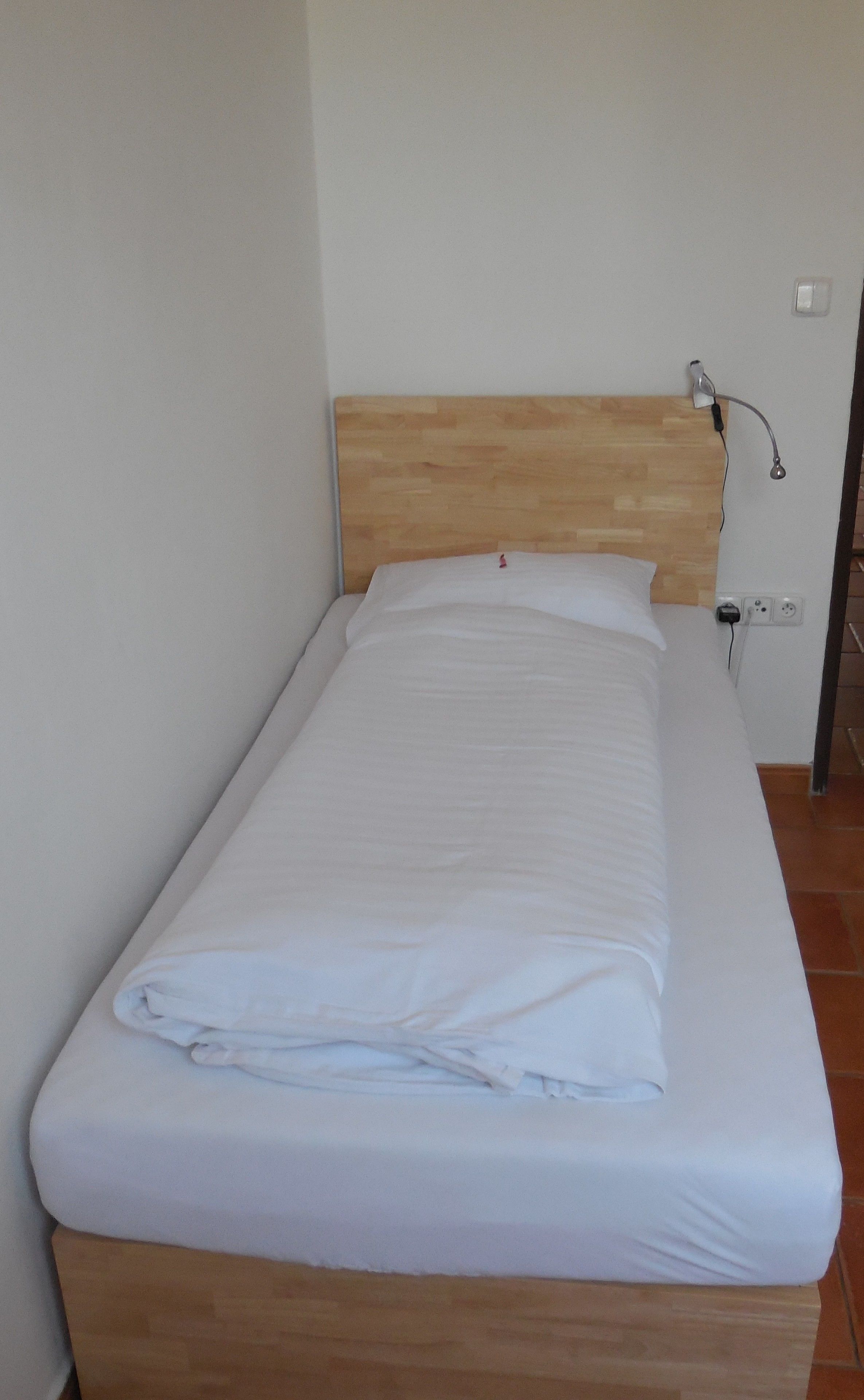 A single bed with a wooden headboard, white bedding, and a bedside lamp.