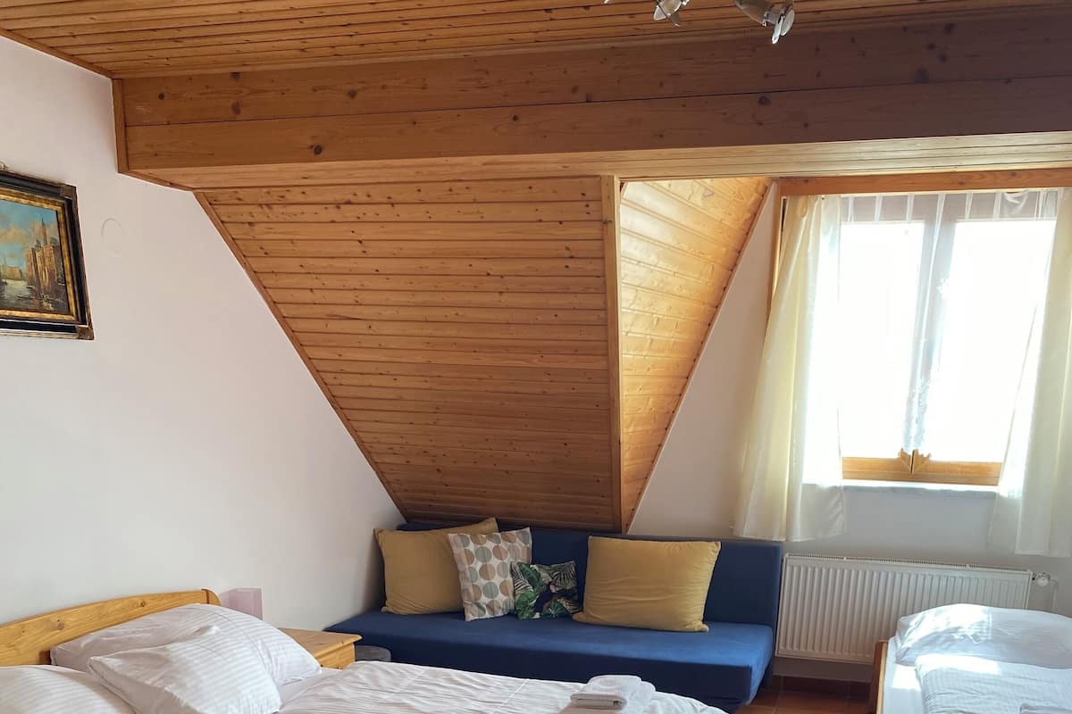 Una habitación acogedora con techo de madera, una cama con ropa blanca impecable, un sofá azul con cojines y una mesita.