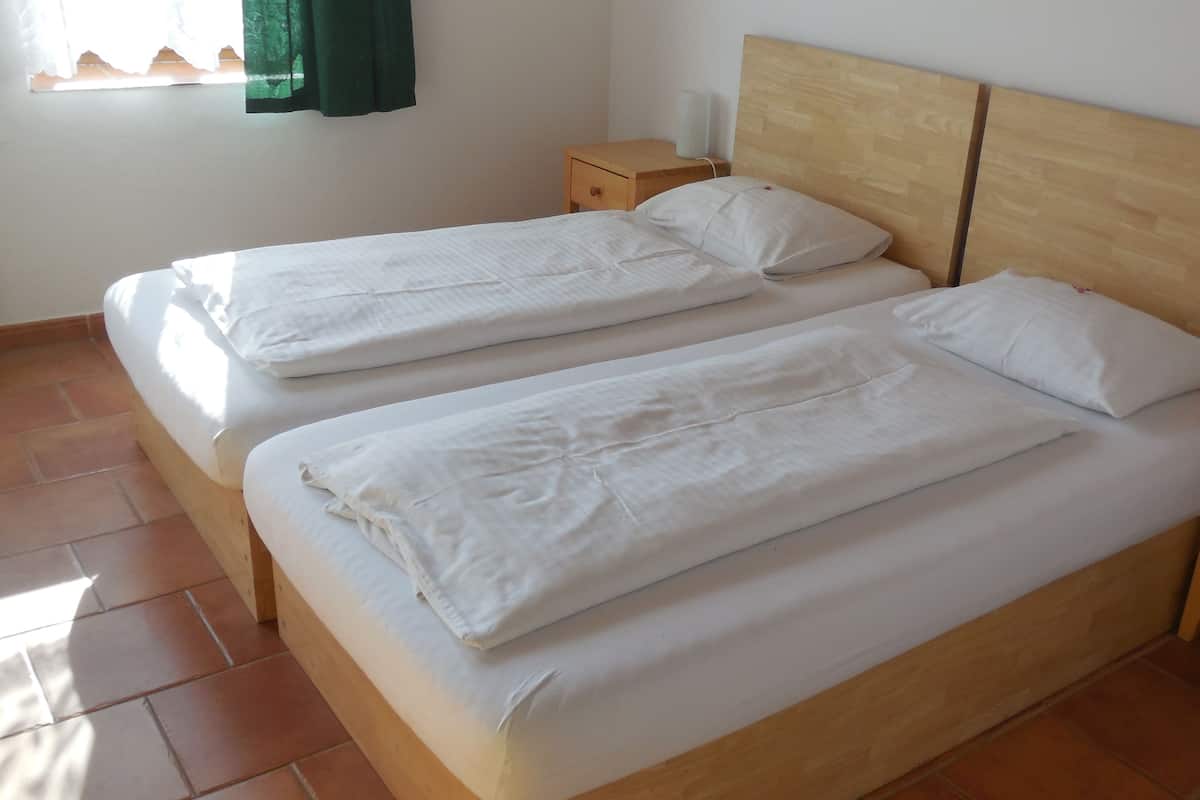 Una cama doble con cabecera de madera, dos mesitas de noche y una ventana con cortina verde.